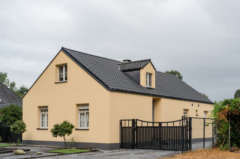 Zijaanzicht van de geïsoleerde woning in Genk met gele gevelpleister en antraciet plint